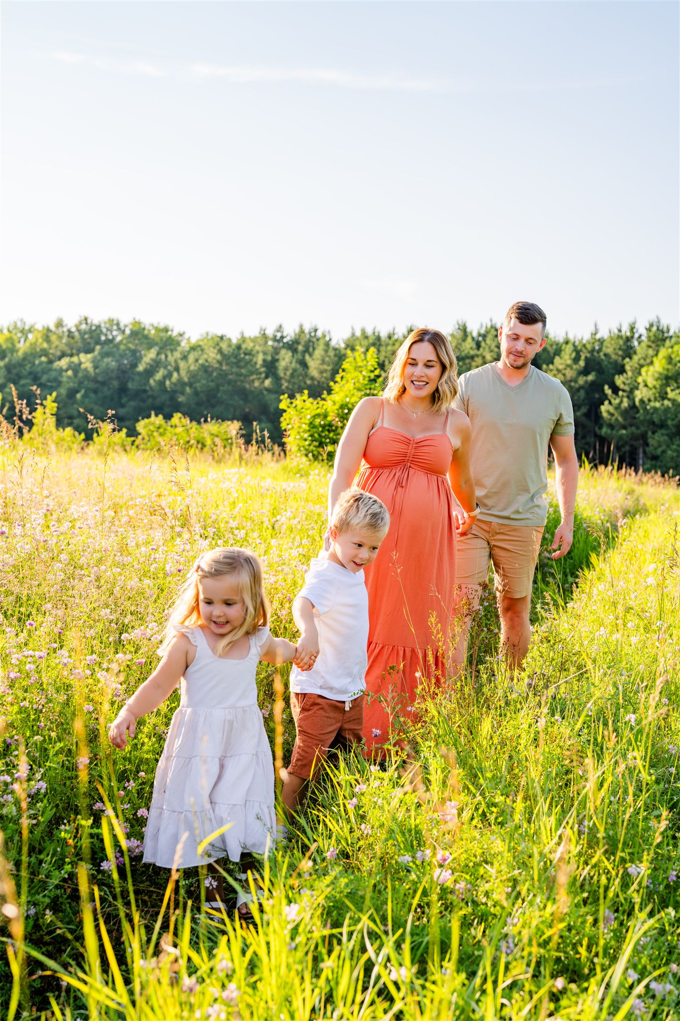 Family of four walking through field during lifestyle maternity session